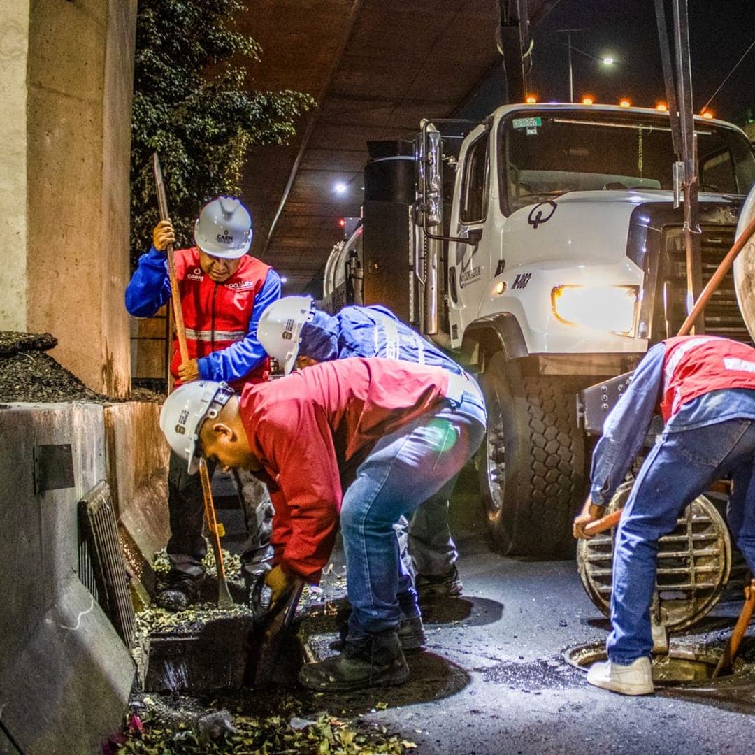 Equipe operando caminhão de hidrojateamento em um poço de visita, à noite.